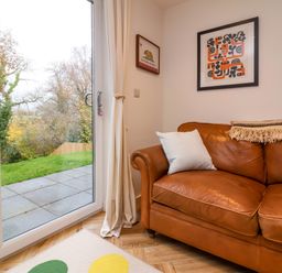 A corner of a room with a brown leather sofa a pillow two framed pictures on the wall and a glass door leading to a garden at Valise in Bideford