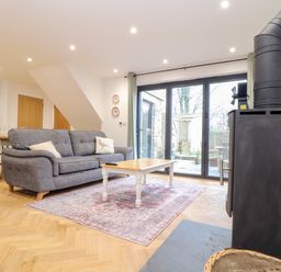 A living room with a grey sofa white coffee table wood burning stove and glass doors leading outside at Wildwood in Newquay