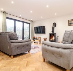 A living room with two grey sofas a wood burning stove and a wall mounted TV at Wildwood in Newquay