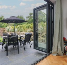 A patio with outdoor dining table and chairs with umbrella in a garden as seen from inside a room at Wildwood in Newquay