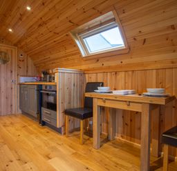 A wooden kitchenette with a stove sink and small dining table with two chairs under a skylight at Heisgeir in Sollas Isle Of North Uist