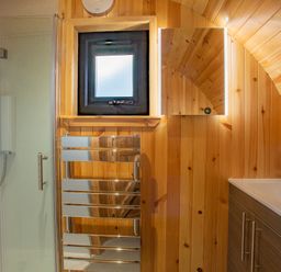 A bathroom with a shower, small window, towel radiator, illuminated mirror, sink, and wooden walls at Heisgeir in Sollas Isle Of North Uist