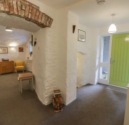 An entryway with a green door and white walls next to a living area with chairs and framed pictures at Le Durkestrete Cellar in Haverfordwest