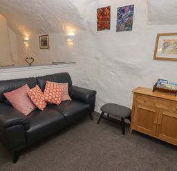 A living room with a black leather sofa and colorful cushions wooden cabinet and framed pictures on white walls at Le Durkestrete Cellar in Haverfordwest