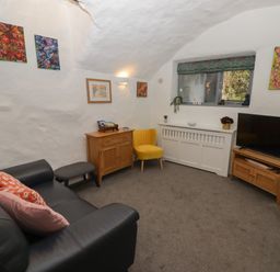 A living room with a black sofa yellow chair wooden cabinets and a TV at Le Durkestrete Cellar in Haverfordwest