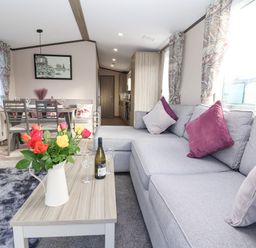 A living room with a gray sofa, a wooden coffee table with flowers and wine, and a dining table with chairs at Ginger Fox Lodge in East Heslerton near Cayton