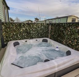 An outdoor hot tub with bubbling water surrounded by privacy screens with leaf patterns at Ginger Fox Lodge in East Heslerton near Cayton