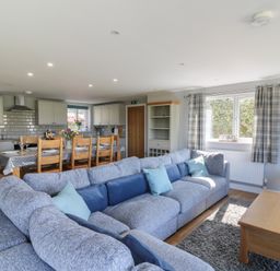 An open living room and kitchen with a large gray sectional sofa, wooden dining table with chairs, and kitchen cabinets at Curtau in Llanfaredd near Builth Wells