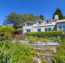 A garden with flowers and bushes in front of a two-story house with multiple windows at Curtau in Llanfaredd near Builth Wells