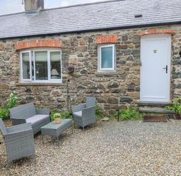 An outdoor seating area with a sofa table and chairs in front of a stone building with white windows and door at The Stables Near Solva