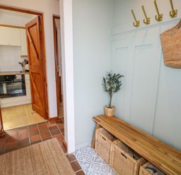 A hallway with wooden bench and baskets with hooks on the wall and a view into a kitchen at The Stables Near Solva