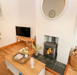 A corner living room with a wood stove fireplace a television on a wooden stand a coffee table with a candle and flowers and baskets with logs near the fireplace at The Stables Near Solva