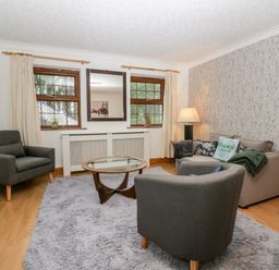 A living room with two grey armchairs a grey sofa a glass coffee table and a lamp at Time and Tide in Arnside