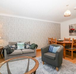A living room with a grey sofa and armchair a wooden dining table and chairs and a glass coffee table at Time and Tide in Arnside