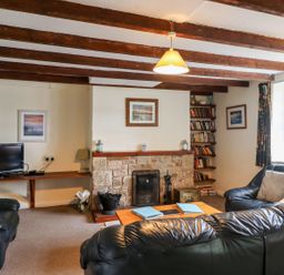 A living room with black leather sofas a wooden coffee table a stone fireplace a wall-mounted wooden shelf with books and a flat screen television at Cherry Tree Cottage Fallodon near Embleton
