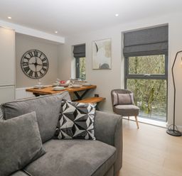 A living room with a gray sofa and patterned pillow next to a dining table set with plates and glasses at Brimstone Backbarrow near Ulverston
