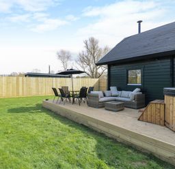 A wooden deck with outdoor seating furniture and a hot tub next to a dark exterior wall of a house in a fenced yard at Squirrel's Nest in South Luffenham near Edith Weston
