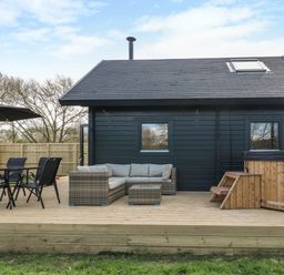 An outdoor patio with a table and chairs umbrella sofa and hot tub at Squirrel's Nest in South Luffenham near Edith Weston