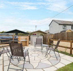 An outdoor patio with four metal chairs around a circular patterned paved area next to a brick barbecue at The Poddy in Bushton near Lyneham