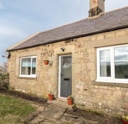 Stone house exterior with a door two windows flower pots on ground and hanging at Moorlaws Farm in Alnwick