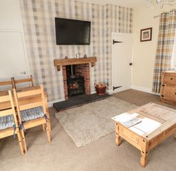 A living room with a wood burning stove under a wall mounted television and wooden furniture at Moorlaws Farm in Alnwick