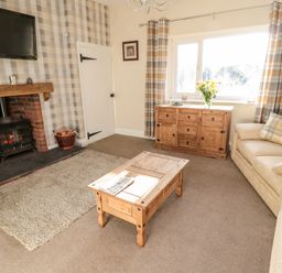 A living room with a wood burning stove TV wooden furniture and a sofa at Moorlaws Farm in Alnwick