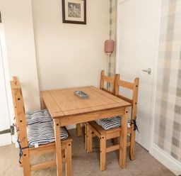 A wooden dining table with four chairs and striped cushions in a room with beige walls and plaid wallpaper at Moorlaws Farm in Alnwick