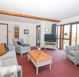 A living room with sofas armchairs a coffee table TV and large windows at Woodland View in Muddiford near West Down