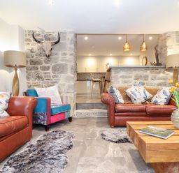 A living room with leather sofas a wooden coffee table and a stone wall with a skull mounted at La Petit Maison in St Columb Major