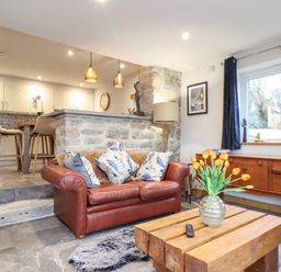 A living room with a leather sofa and wooden coffee table next to an open kitchen at La Petit Maison in St Columb Major