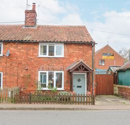 A brick house with a tiled roof and a small front garden behind a wooden fence at Easter Cottage in Dersingham