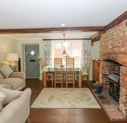 A living room with sofas a dining table a brick fireplace and wooden beams at Easter Cottage in Dersingham