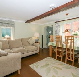 A living room with a beige sofa a wooden dining table with chairs and a lamp at Easter Cottage in Dersingham
