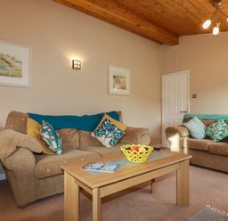 A living room with two beige sofas and a wooden coffee table with a fruit bowl and magazines at 4 The Glade in St Minver