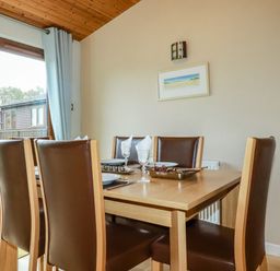 A dining room with six brown leather chairs around a wooden table set for a meal at 4 The Glade in St Minver