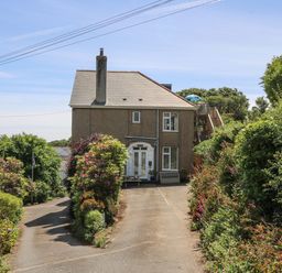 A two-story house with a driveway surrounded by bushes and flowers at Godrevy in Porthcurno