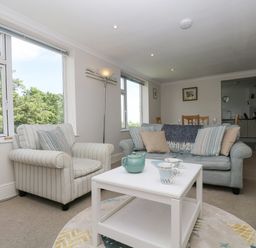 A living room with a striped armchair a sofa with cushions and a white coffee table with a teapot at Godrevy in Porthcurno