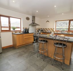 A kitchen with wooden cabinets a black countertop a stainless steel refrigerator stove and three metal bar stools at Y Tylwyth in Blaenau Ffestiniog