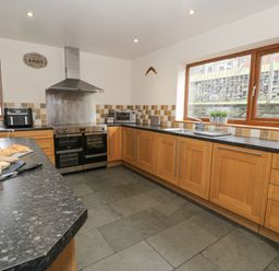 A kitchen with wooden cabinets black countertops double oven microwave and large windows at Y Tylwyth in Blaenau Ffestiniog