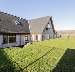 A fenced yard with grass next to a house with a sloped roof and stone wall at Y Tylwyth in Blaenau Ffestiniog