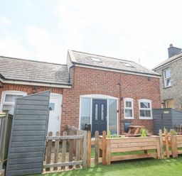 A brick house with a dark blue door and small garden beds with plants in front at Pine Cottage in Dinas Dinlle