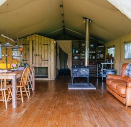 An interior of a tent with a wooden dining table and chairs a wood stove shelves with kitchen items and a brown leather couch at Oak Stockland near Dalwood