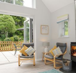 A sitting area with two chairs and cushions next to a wood stove and open doors leading to an outdoor patio at Otters Leap in Bideford
