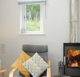 A chair with two cushions next to a side table with a lamp and a fireplace with fire at Otters Leap in Bideford