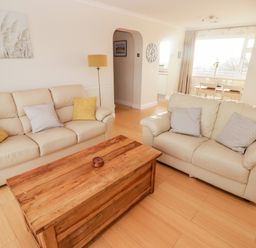 A living room with two beige sofas a wooden coffee table and a dining table near a window at 54 Croft Court in Tenby