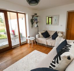 A living room with two sofas pillows wooden floor glass door and small tables at Little Rondeval in Totnes