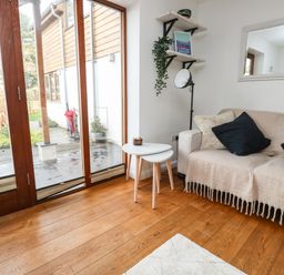 A seating area with a sofa covered by a throw blanket and cushions beside nested side tables and large glass doors at Little Rondeval in Totnes