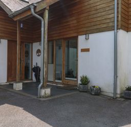 An exterior view of a building entrance with wooden doors glass panels a covered porch and potted plants at Little Rondeval in Totnes