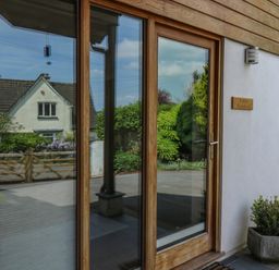 A wooden framed glass door with adjacent window and plants outside at Little Rondeval in Totnes