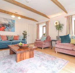 A living room with blue and pink sofas cushions a wooden coffee table and abstract painting at Riviere Barton in Hayle